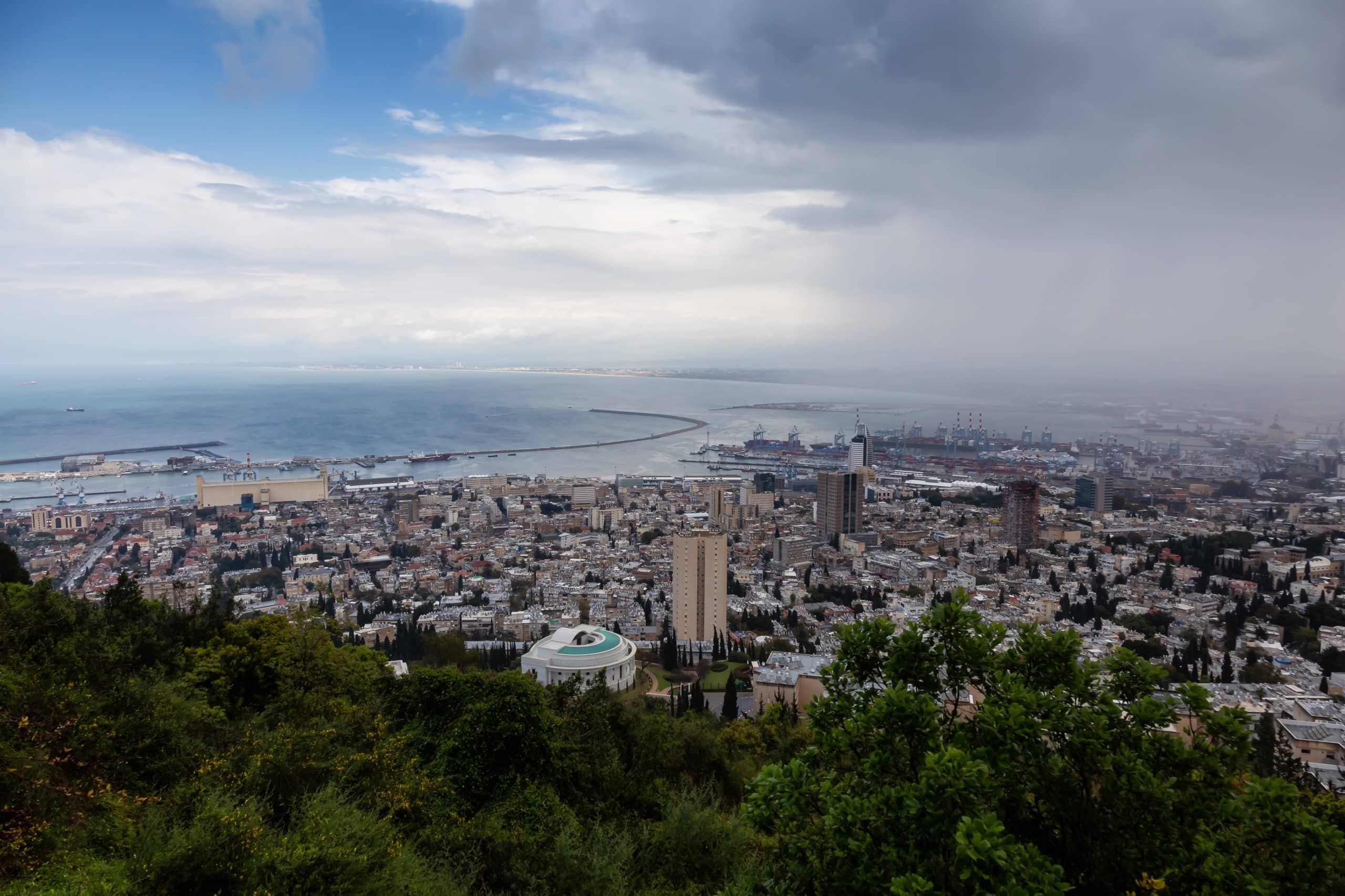 תמונה אוירית של העיר חיפה ונמל חיפה ברקע. עננים רבים בשמיים